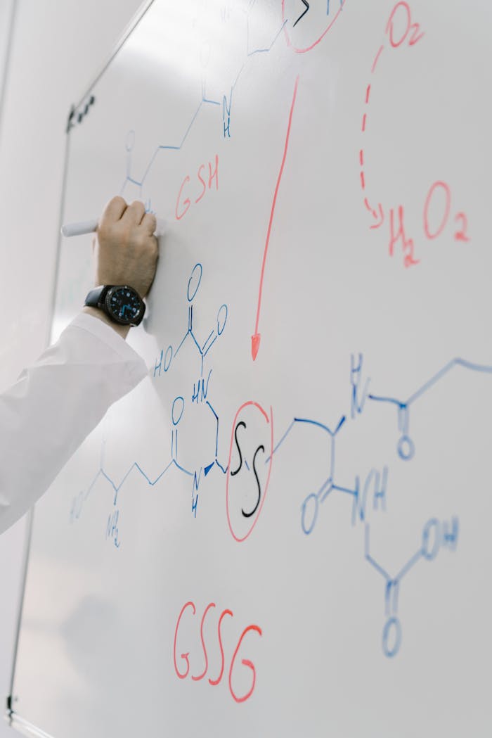 Scientist writing complex chemical formula on a whiteboard during a lab session.